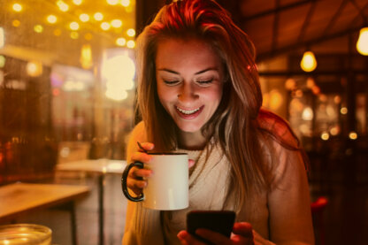 A young woman enjoying a hot beverage is checking something on her phone. A young woman enjoying a hot beverage is checking something on her phone.