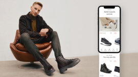 A man sitting on a chair, showing off his shoes. Next to him, there's a smartphone opened on the eobuwie app. A man sitting on a chair, showing off his shoes. Next to him, there's a smartphone opened on the eobuwie app.